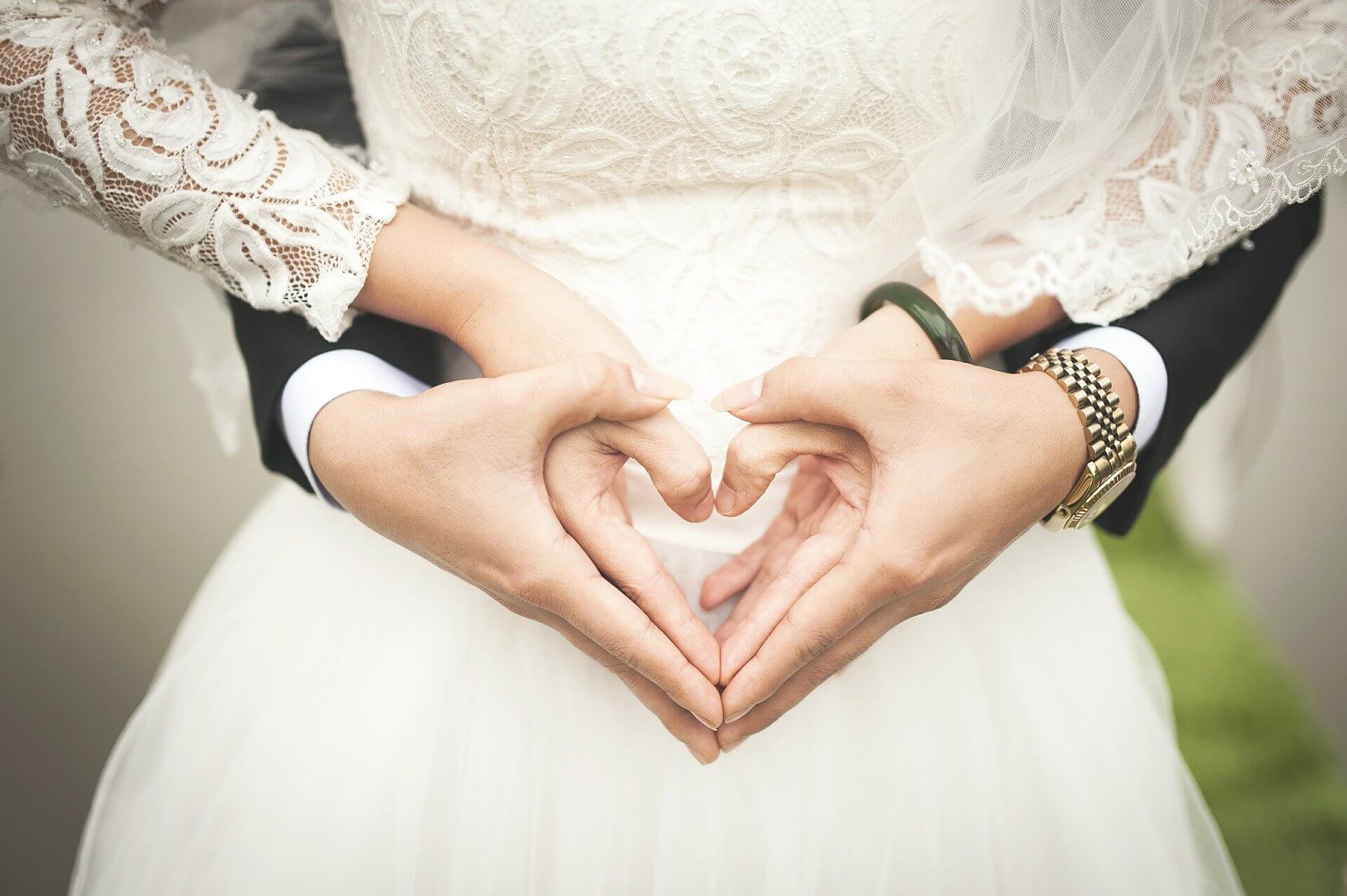 A man and woman at a wedding with hands held in a heart shape