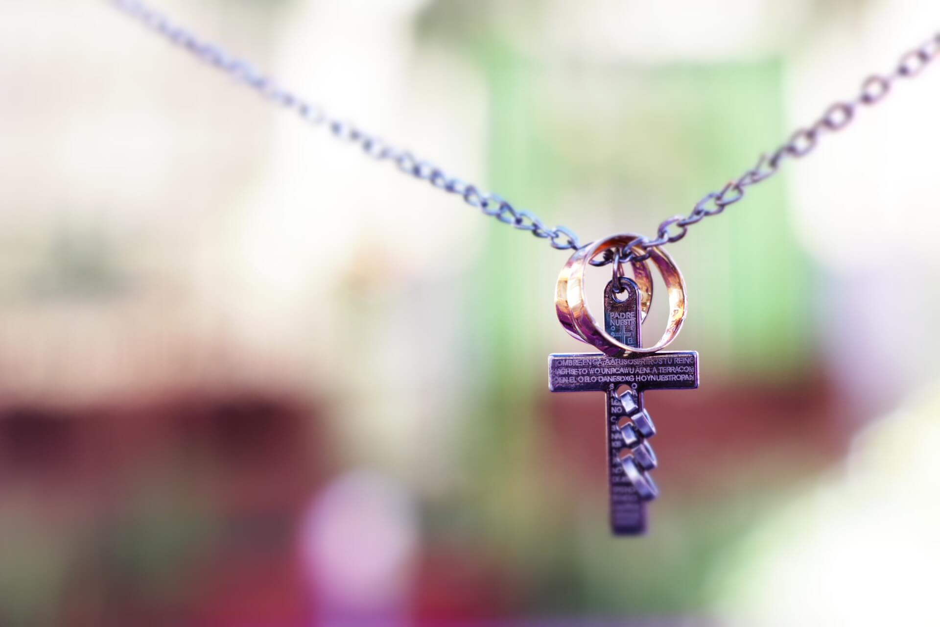 A necklace holding a cross and wedding bands