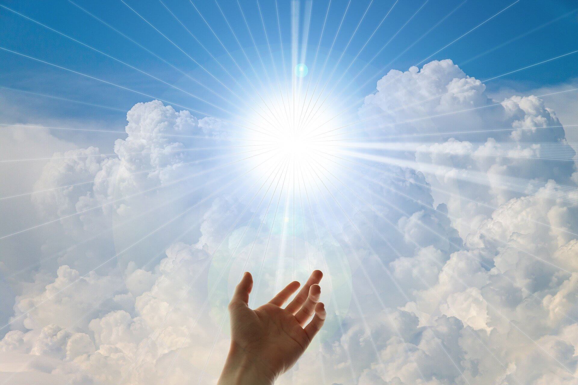 a hand reaching up to the sun’s rays coming through clouds