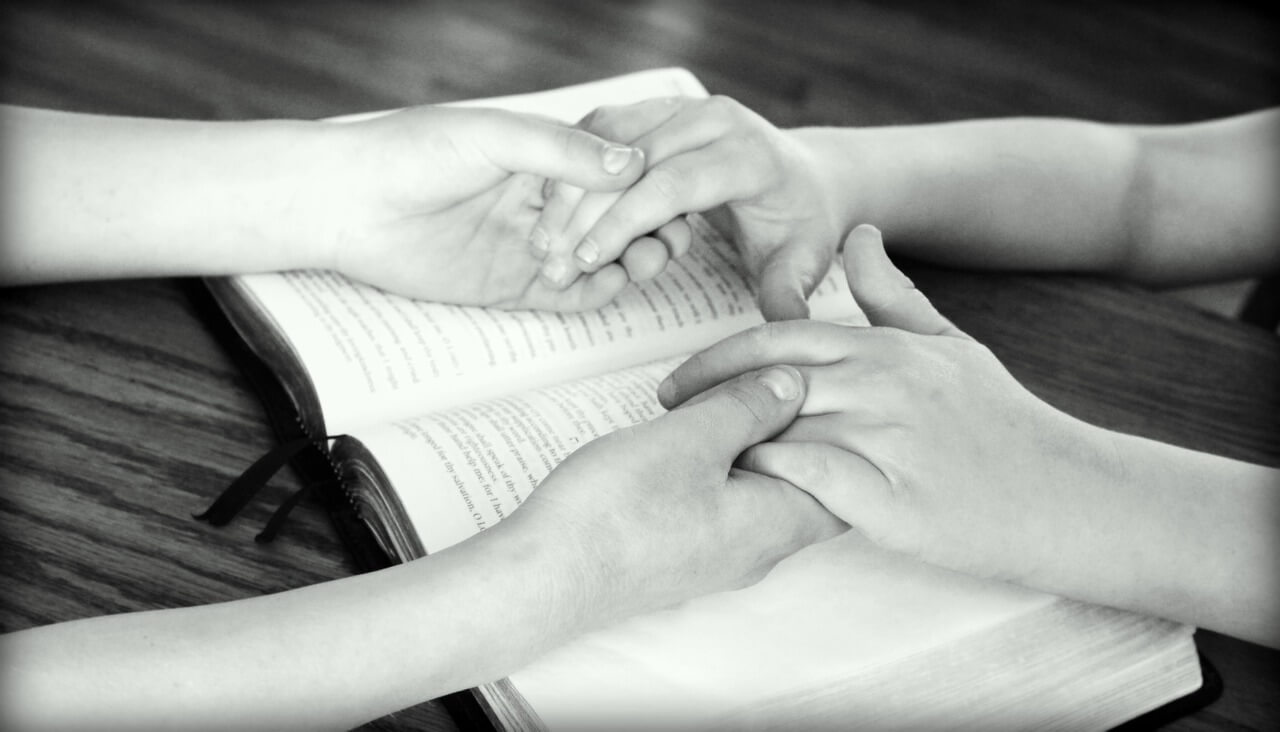 a black-and-white image of two people holding hands over a Bible