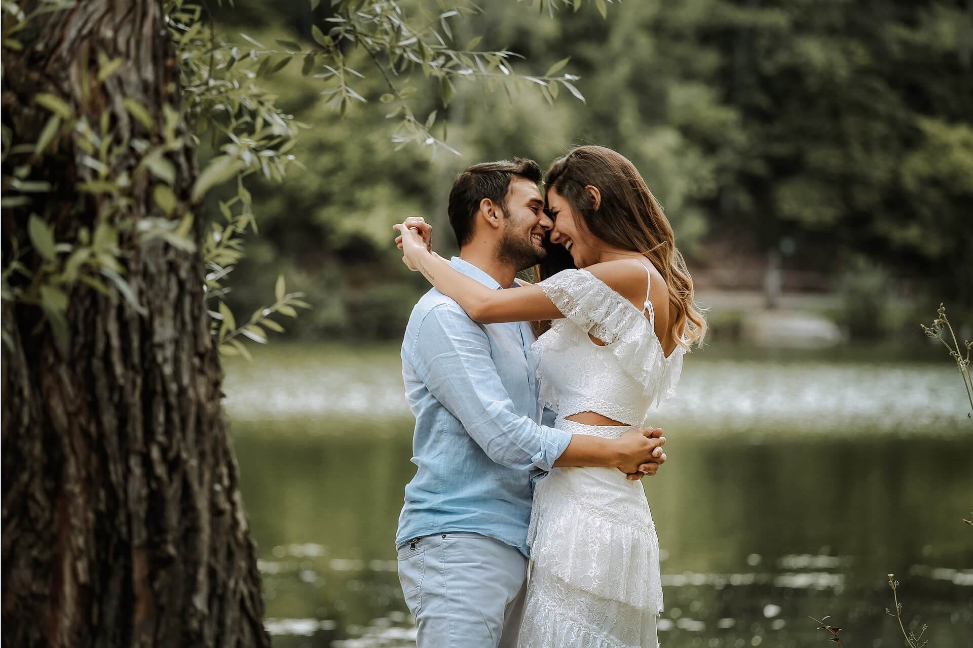 a man and woman smiling and embracing next to a pond