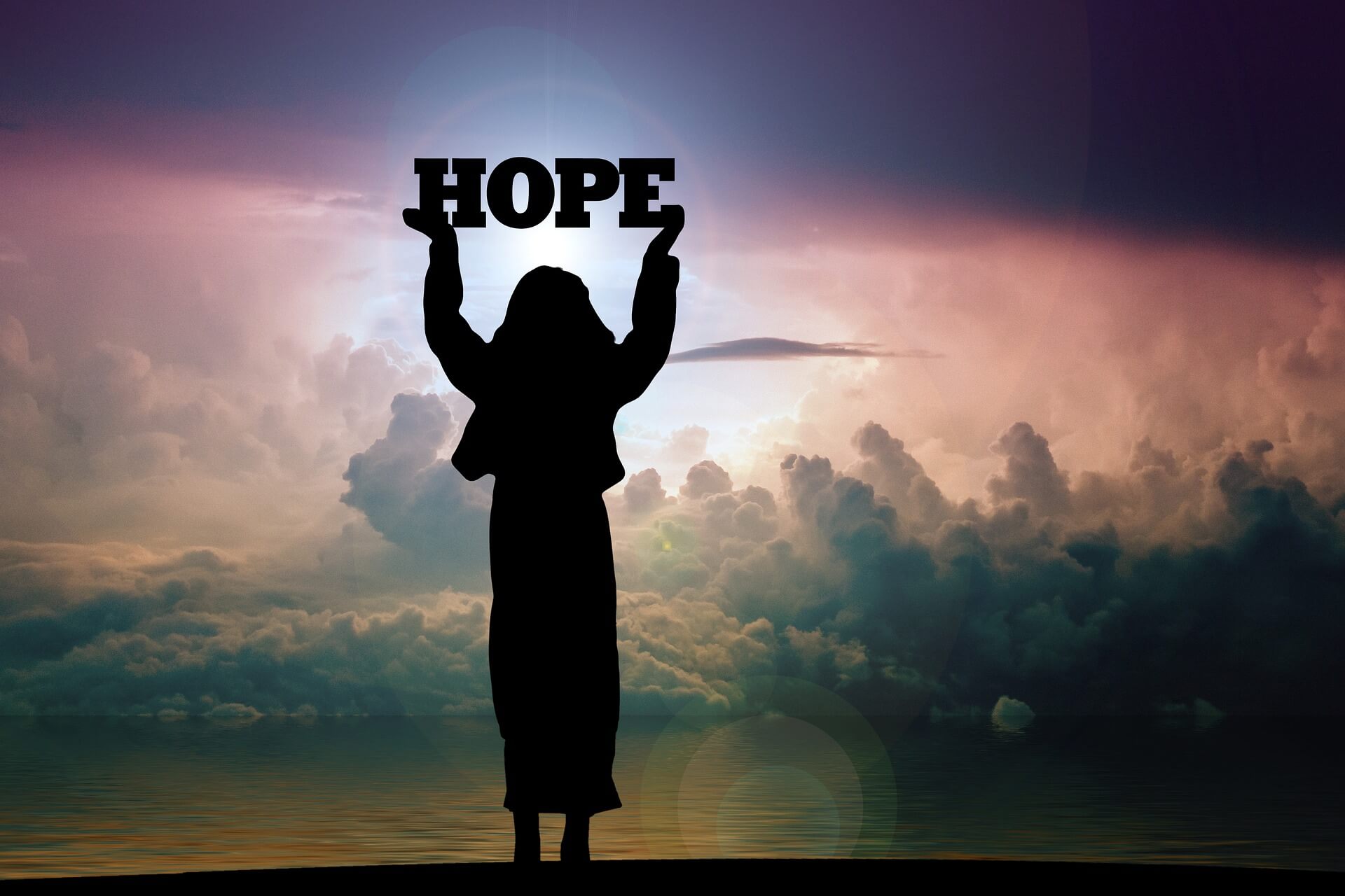 The silhouette of a woman holding the word hope in front of the sky