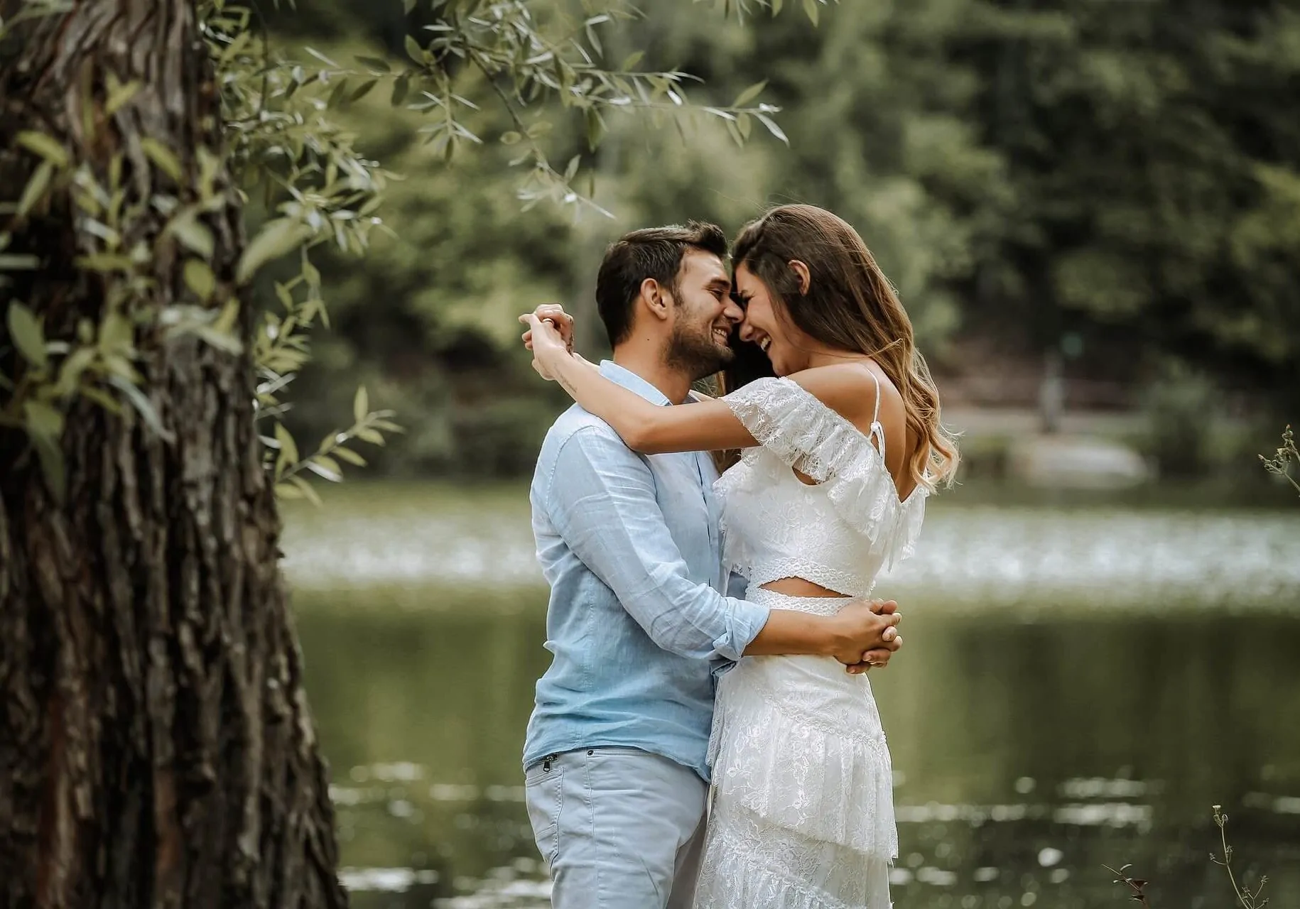 a man and woman smiling and embracing next to a pond