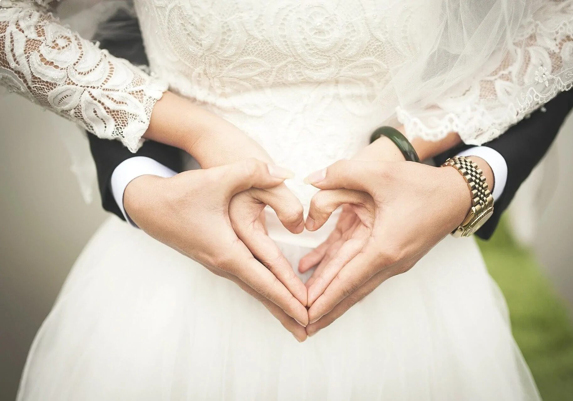 A man and woman at a wedding with hands held in a heart shape